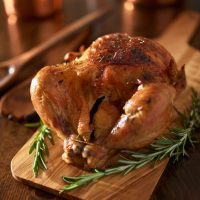 rotisserie chicken on wooden serving tray with herbs and rosemary